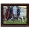 This western style art is a closeup of two people wearing cowboy boots resting on a fallen tree - Framed Canvas